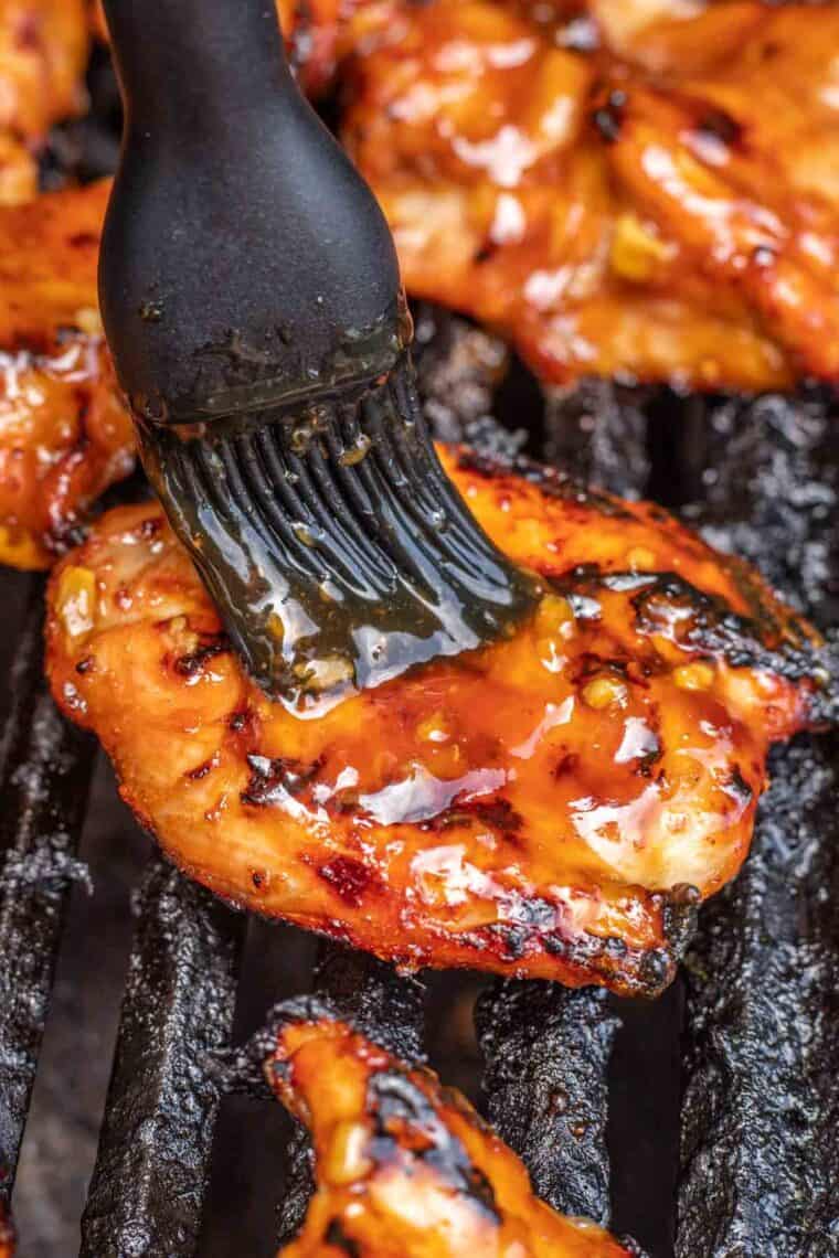 Teriyaki chicken on a grill being brushed with teriyaki sauce. 