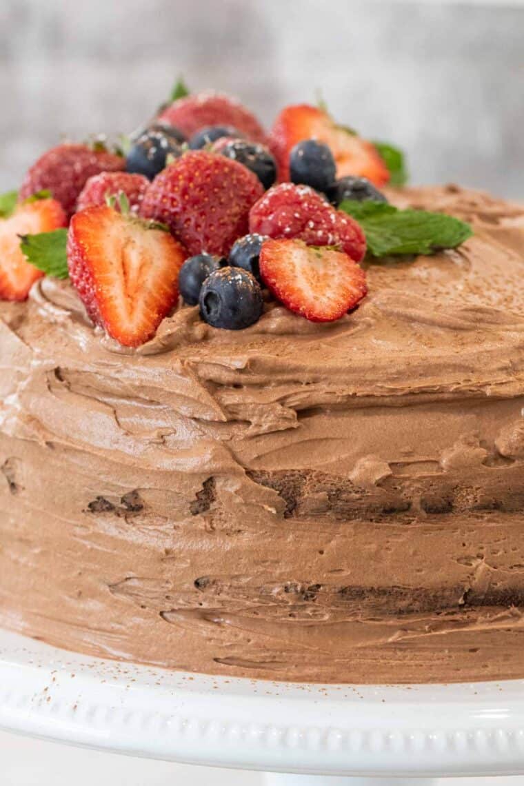 Chocolate mousse cake on a white cake stand topped with fresh berries. 