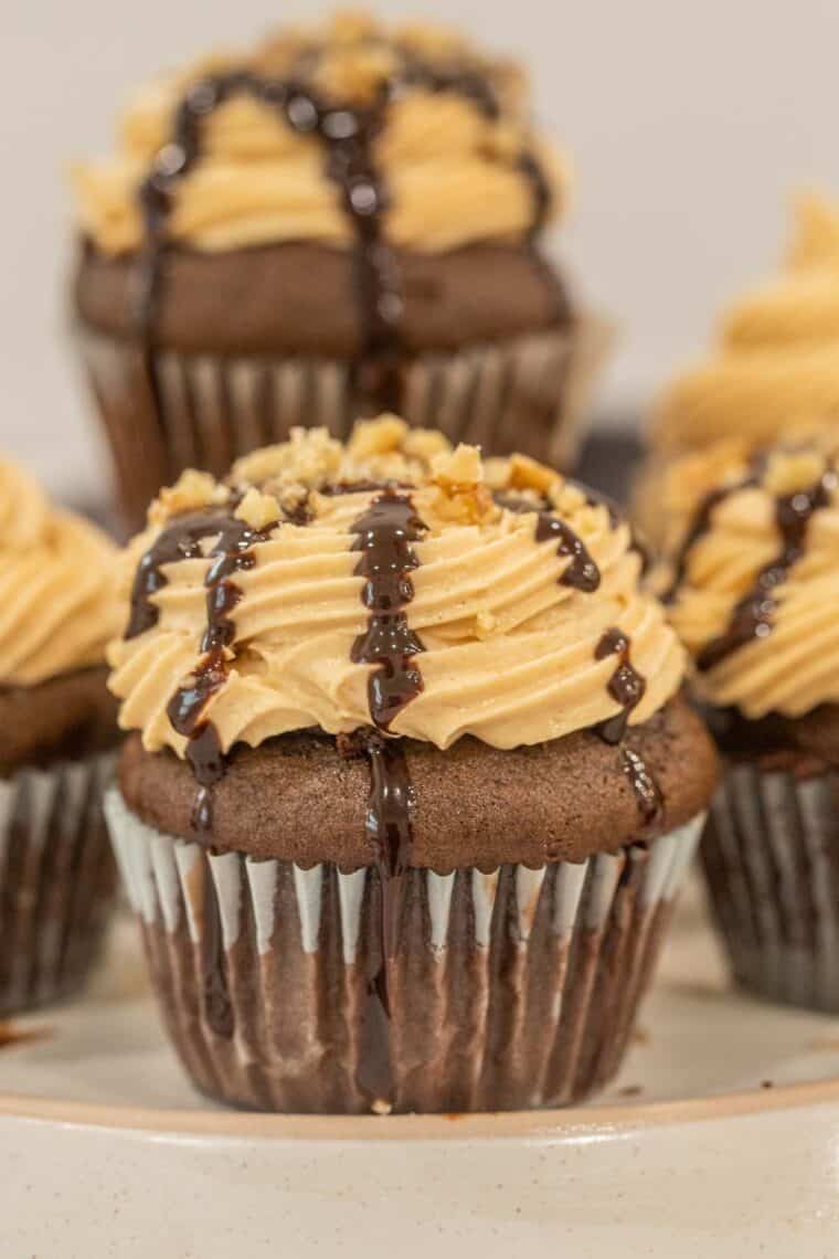 Chocolate peanut butter cupcakes on a plate topped with chocolate ganache and chopped walnuts. 