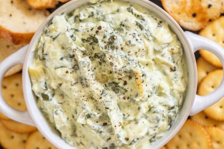 Creamy spinach artichoke dip in a white bowl with crackers. 