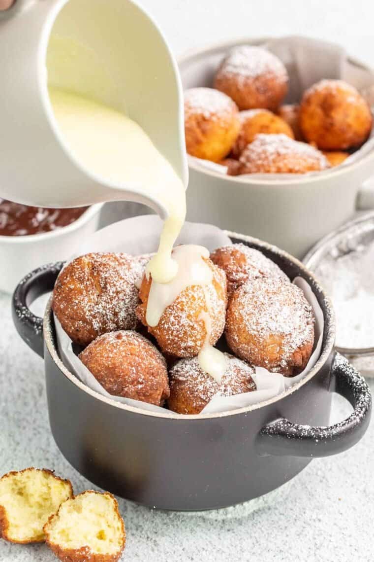 Donut holes in a bowl with condensed milk being drizzled over. 