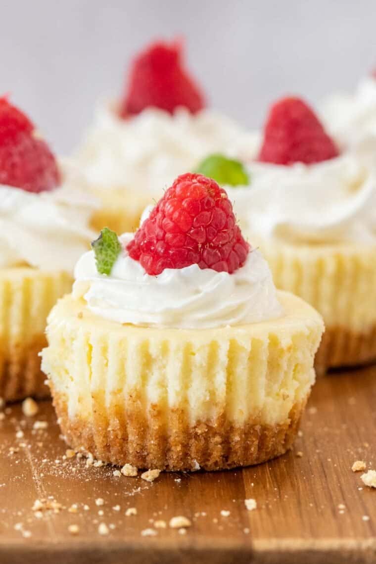 Cheesecake bites on a cutting board topped with whipped cream and fresh raspberries. 