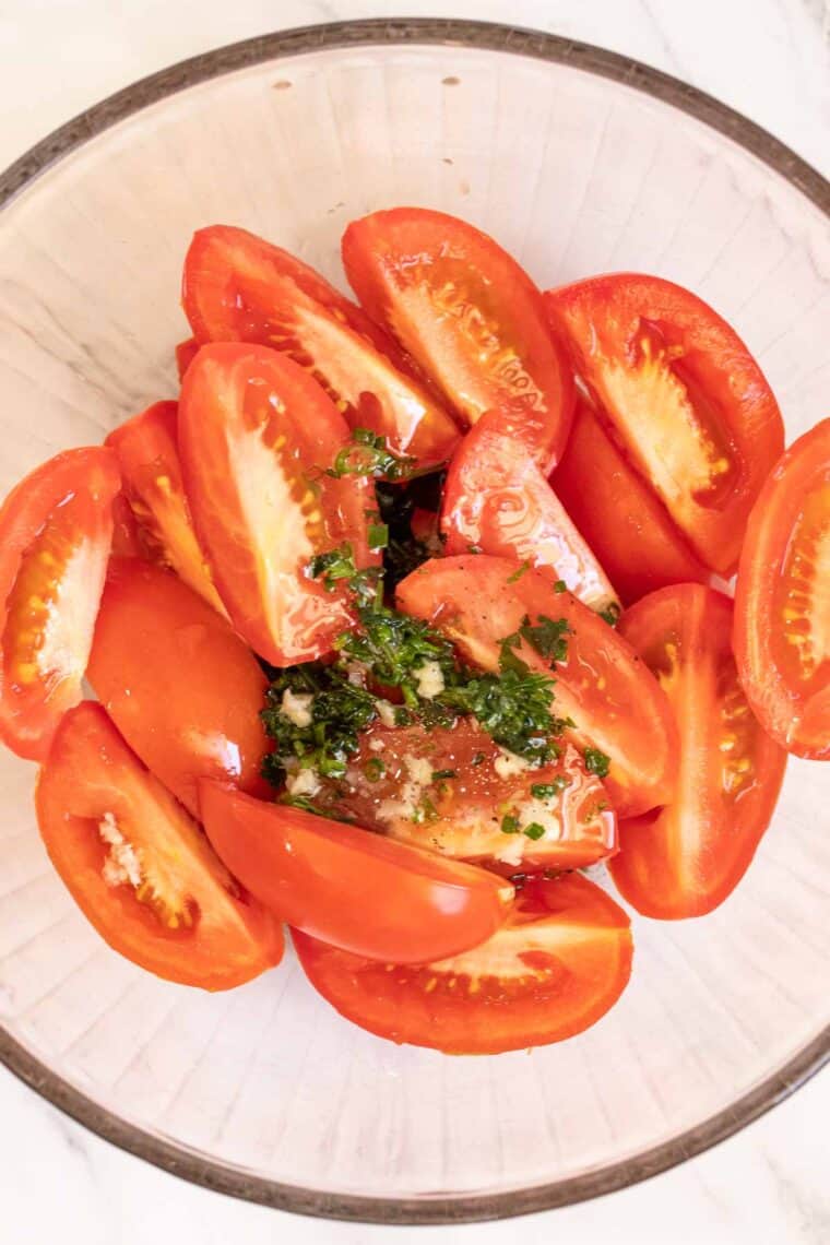 A glass bowl with sliced tomatoes and  the marinade over the tomatoes. 