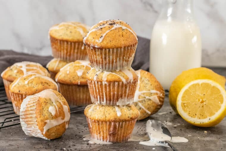 Lemon poppyseed muffins stacked on top of each other next to lemons and milk. 