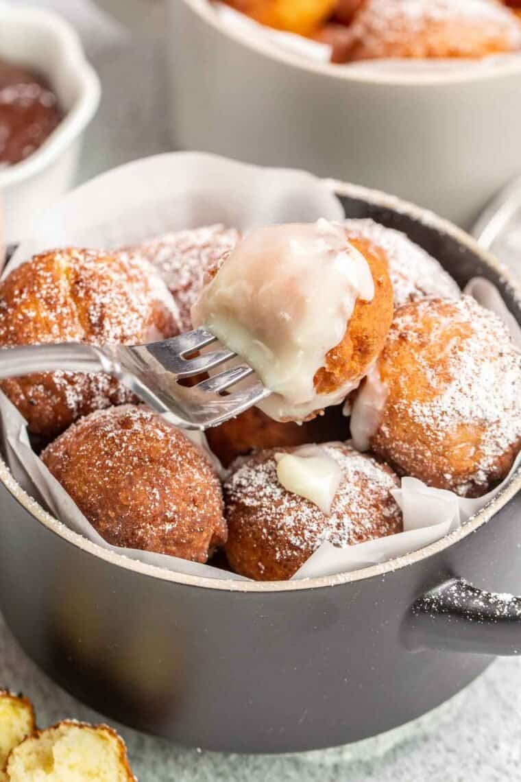 A fork holding a ricotta donut topped with powdered sugar and condensed milk. 