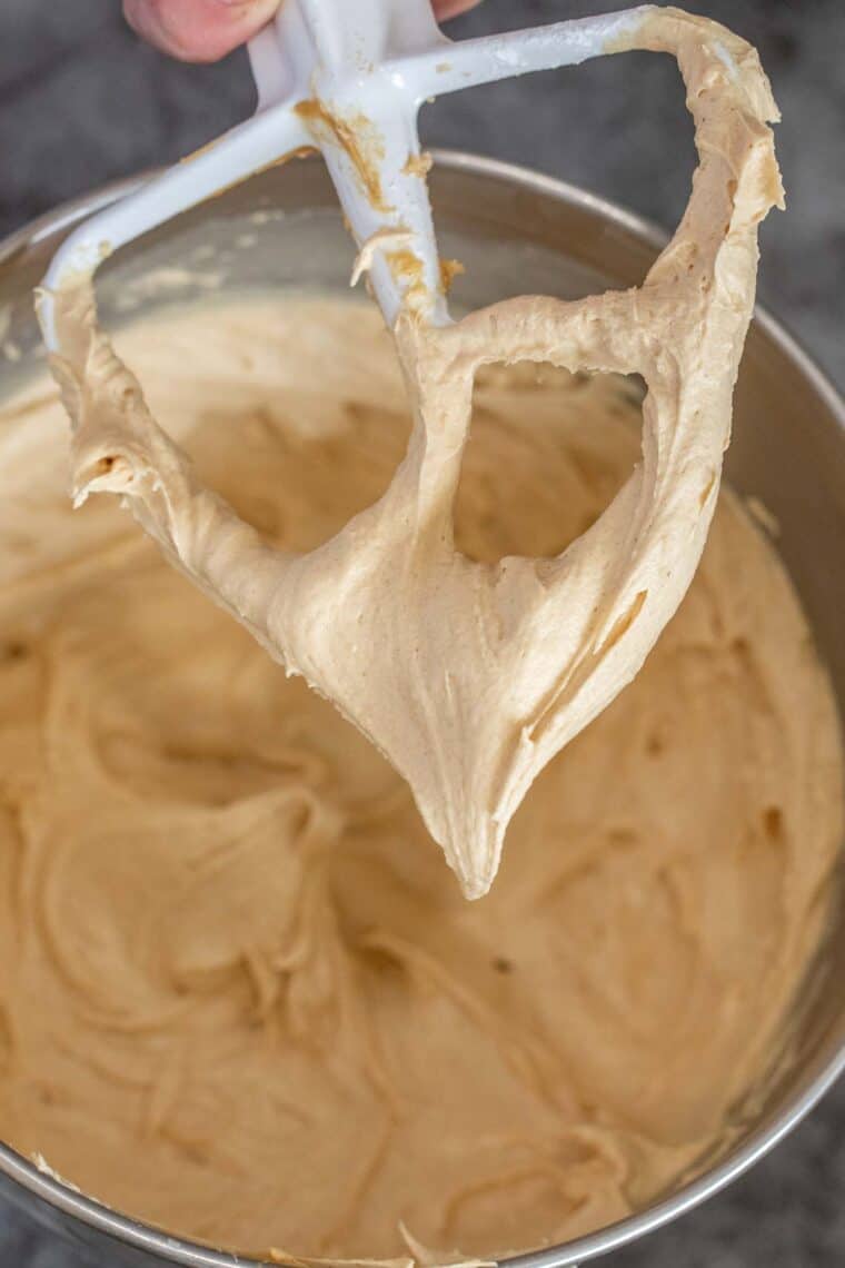 Peanut butter frosting with a ladle being held with frosting. 