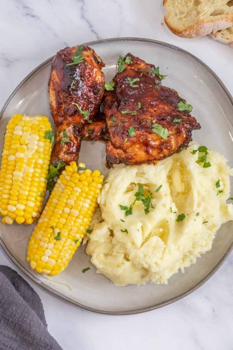 Bbq grilled chicken on a plate with creamy mashed potatoes and corn on the cob. 