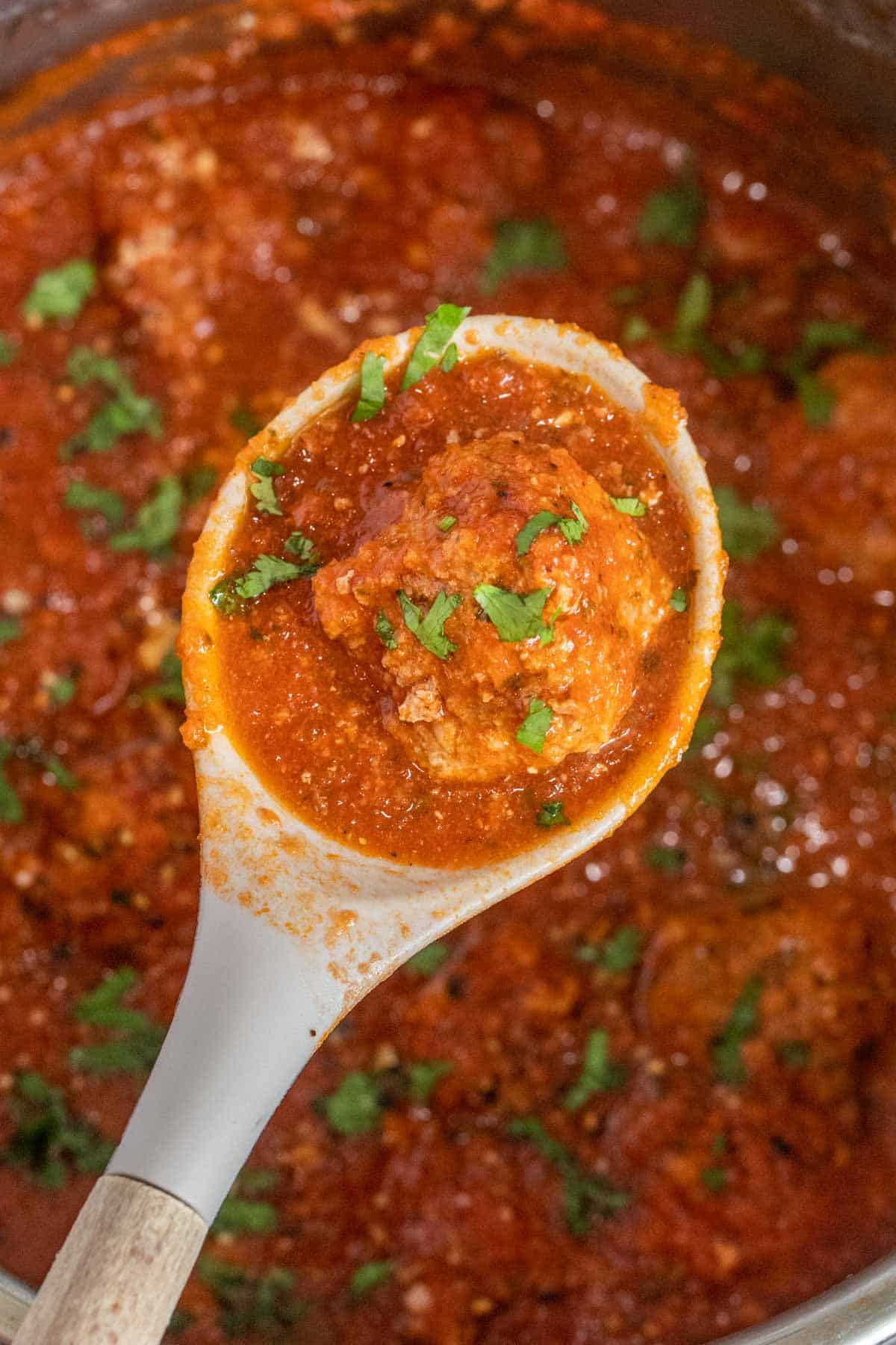 A ladle with instant pot meatballs topped with fresh greens, 