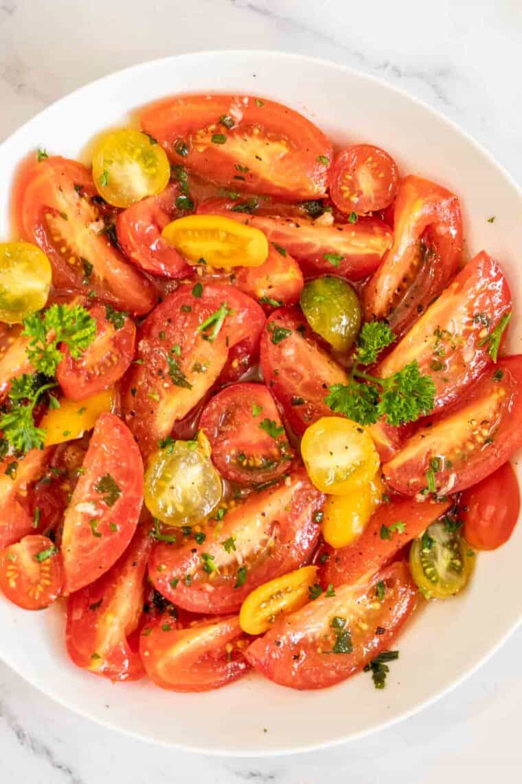 A white bowl with marinated tomatoes topped with fresh greens. 