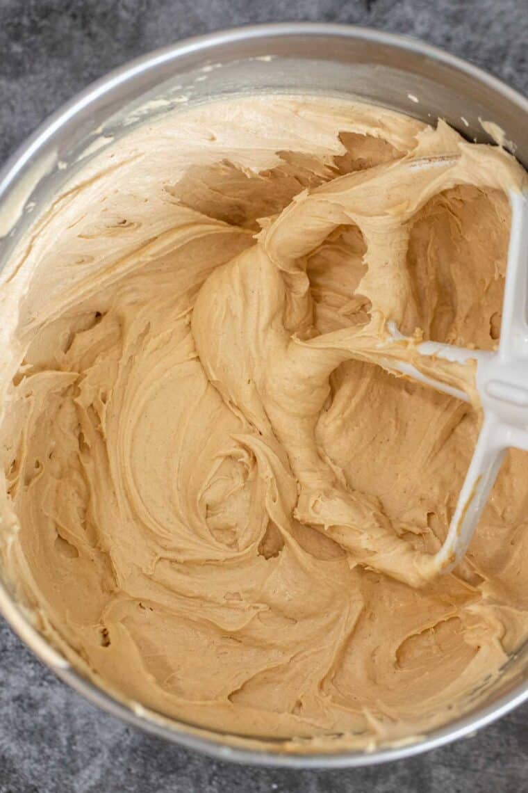 A bowl of cremy peanut butter frosting with mixer attachment. 