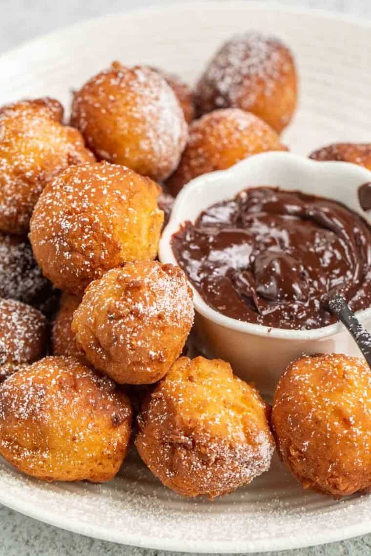 A plate of ricotta donuts next to a white bowl of chocolate sauce. 