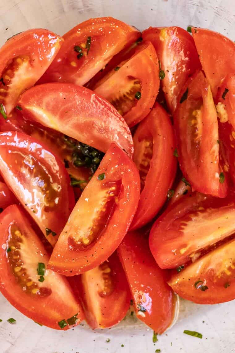 Tomatoes marinating in a glass bowl.