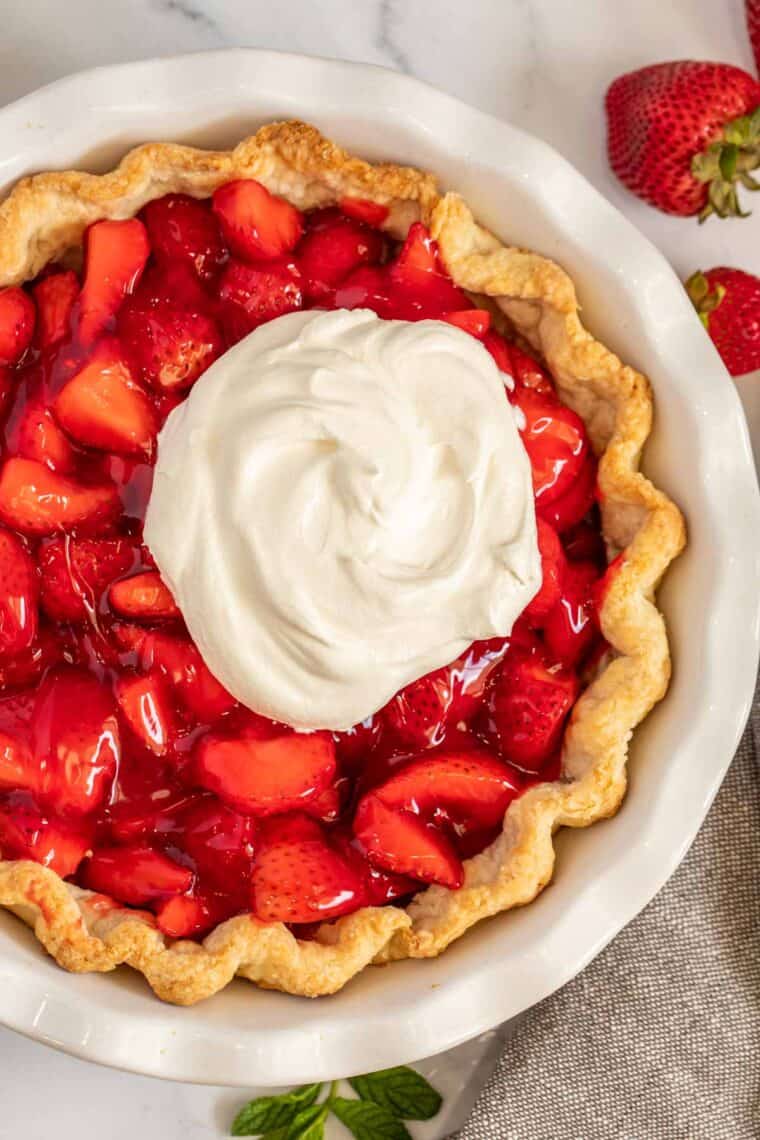Strawberry cream pie in a white pie dish loaded with whipped cream. 