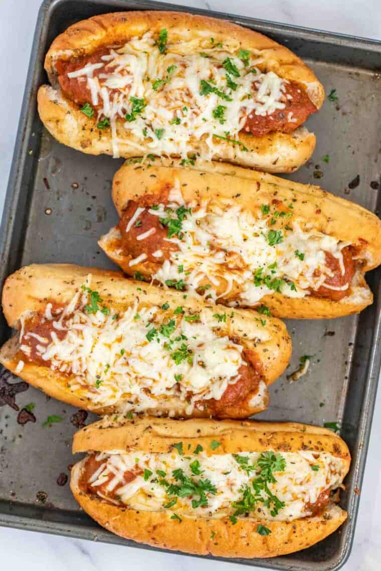 Four meatball subs on a baking sheet topped with freshly chopped greens. 