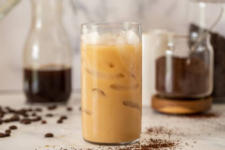 Iced coffee in glass with ice next to pitcher of cold brew and coffee beans. 