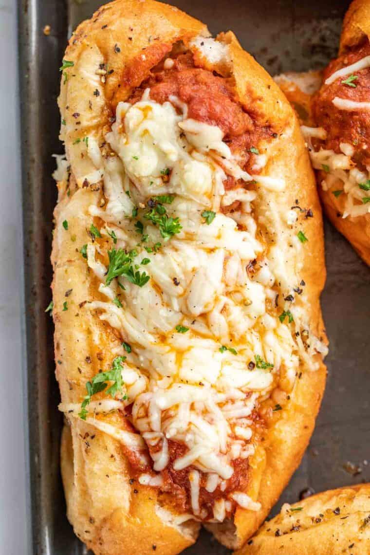 Meatball sub on a baking sheet toppe with freshlt chopped parsley. 