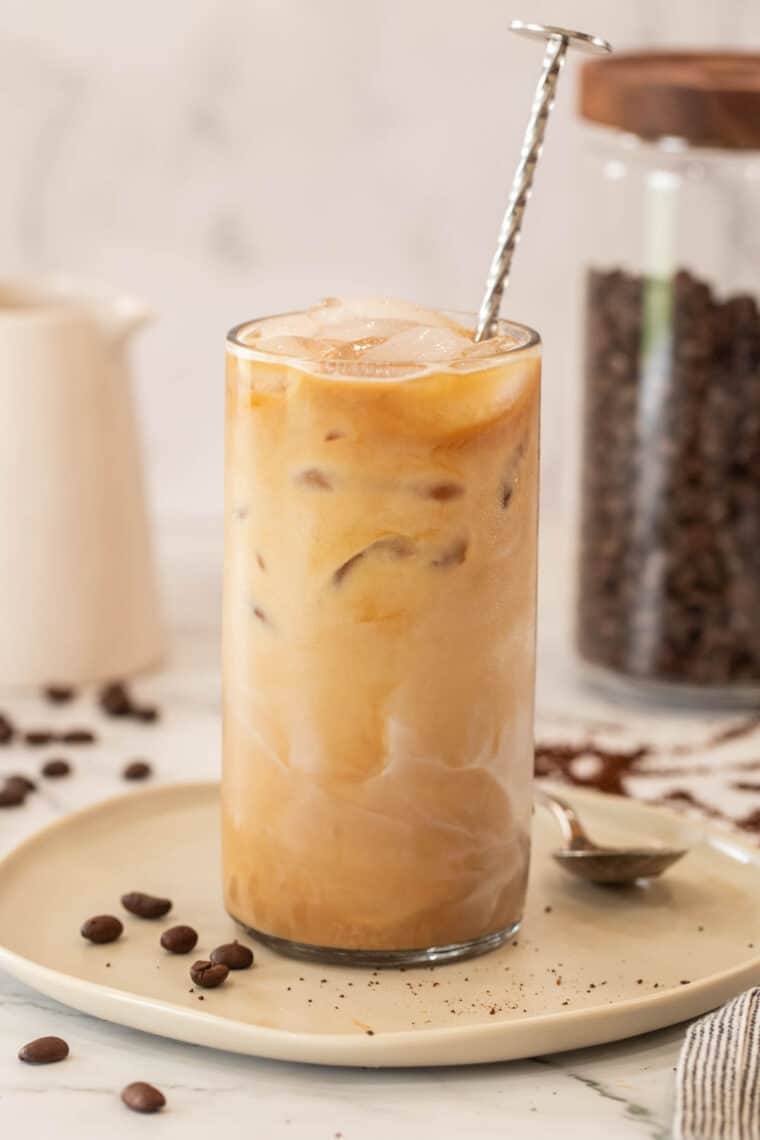 Iced caramel macchiato in a glass cup with ice and a metal spoon. 