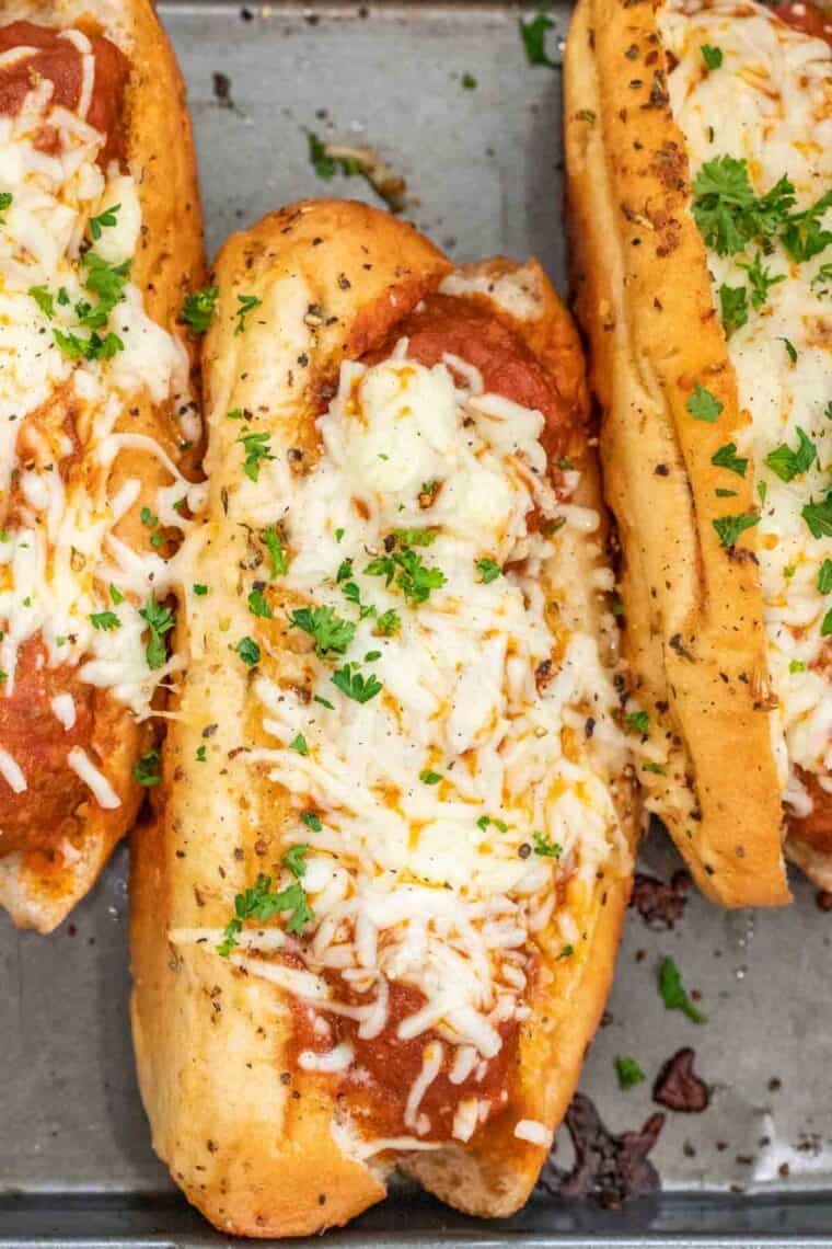 Meatball sub sandwiches on a baking sheet topped with chopped greens. 