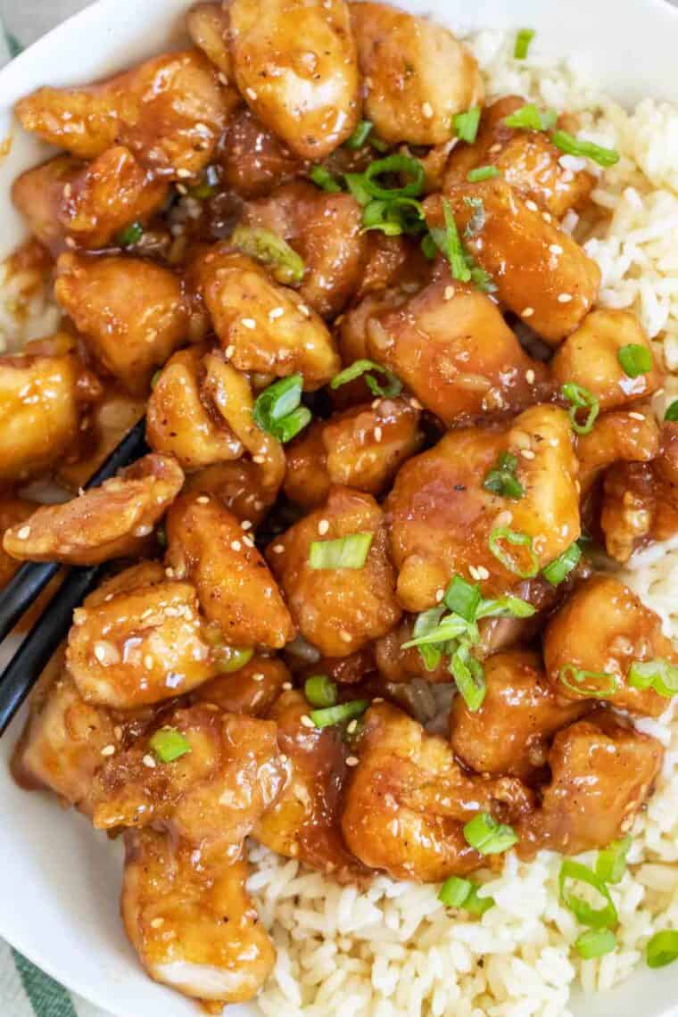 Orange chicken over a bed of rice topped with freshly chopped green onion and sesame seeds.