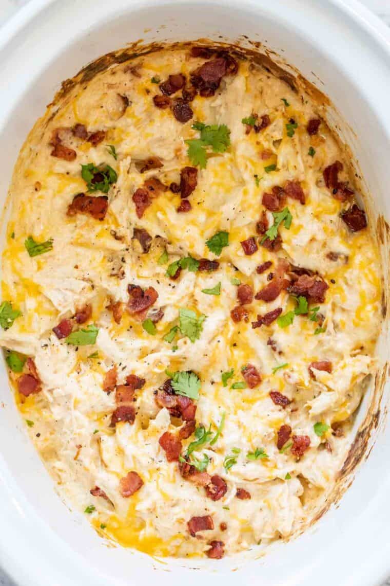 Ranch Chicken recipe in a crockpot topped with bacon and herbs.