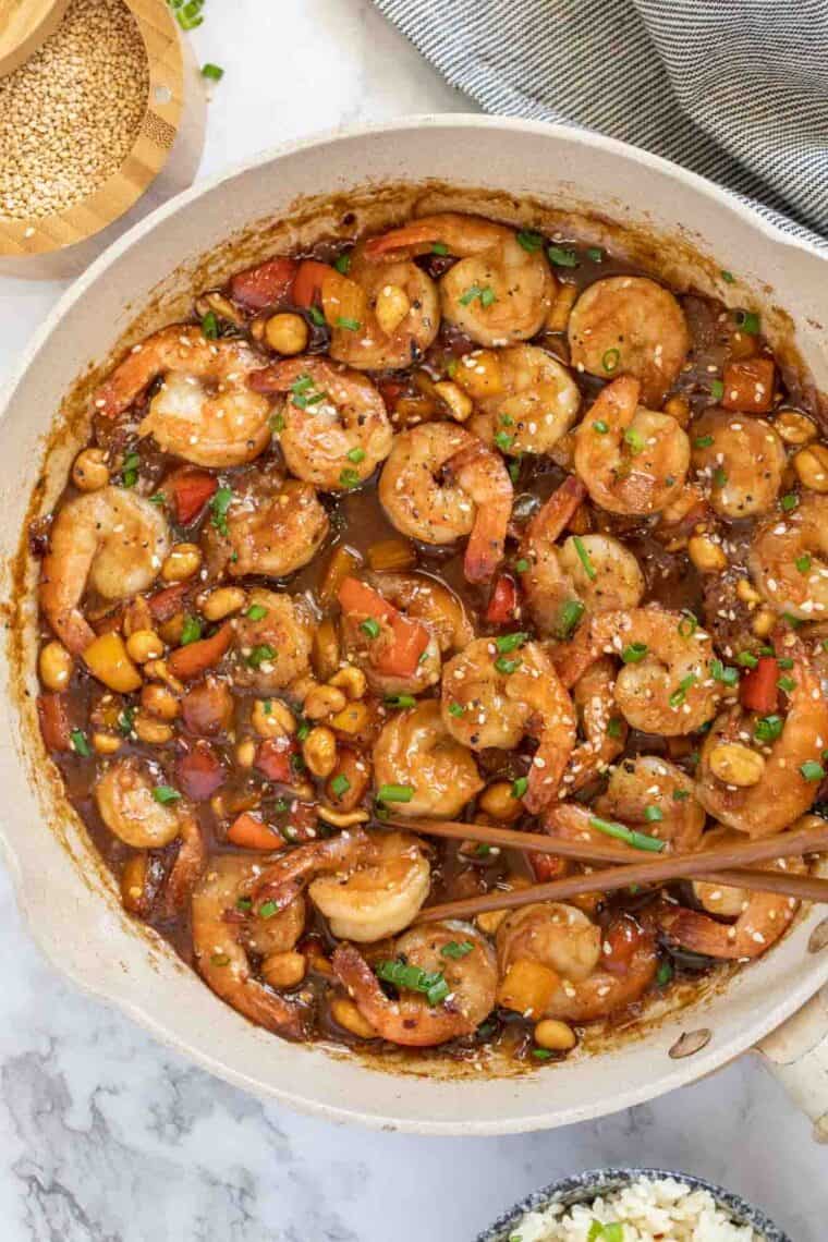 A skillet filled with kung pao shrimp topped with green onion. 
