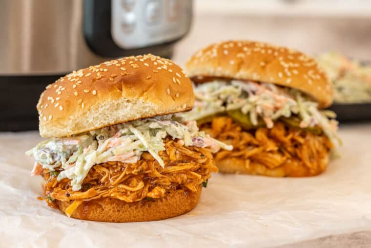 Two BBQ chicken breast sandwiches with instant pot in the background.
