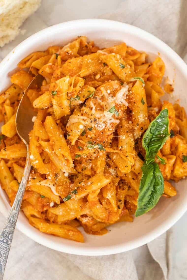 Pasta in a bowl tossed with marinara and basil.