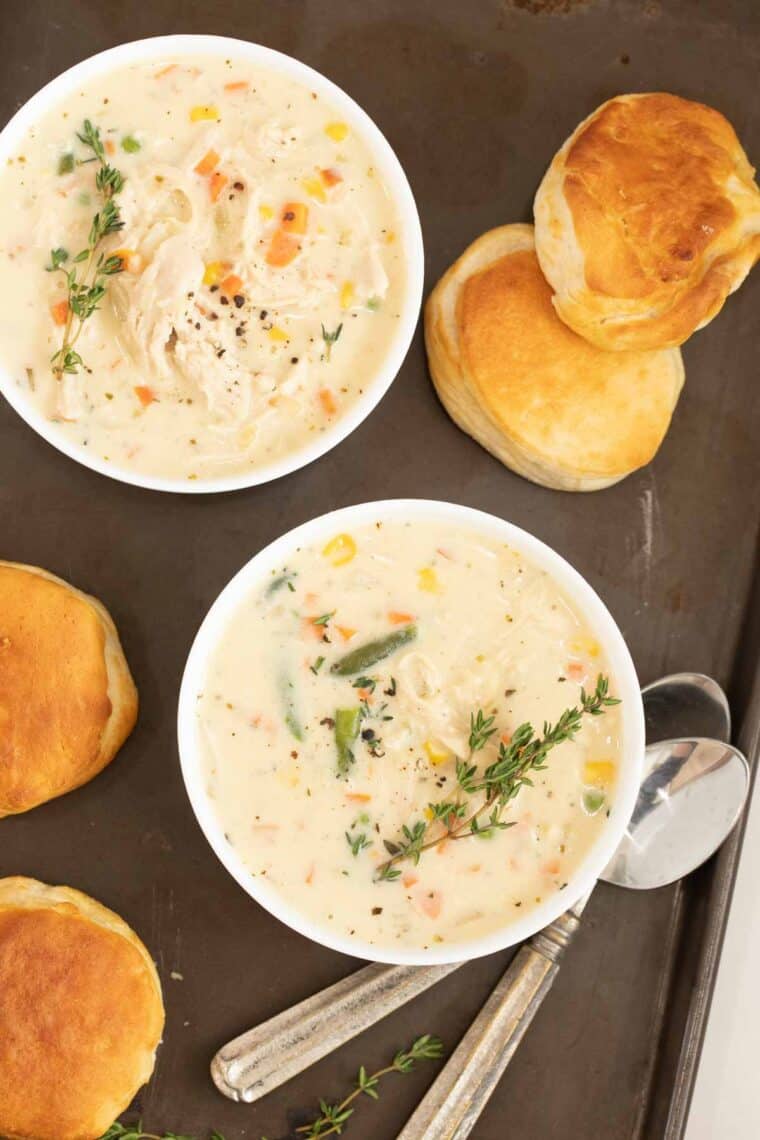 Two bowls of Chicken Pot Pie with bread and spoons on the side.