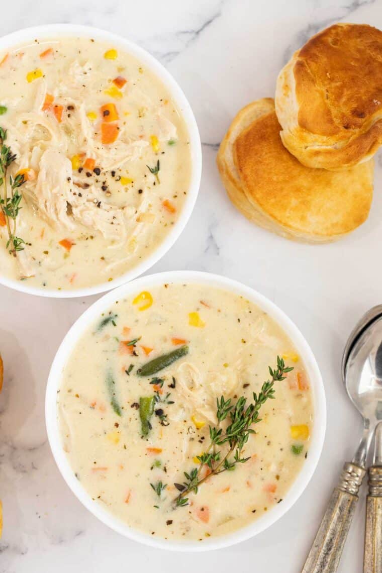 Chicken pot pie in bowls topped with thyme and bread next to the bowls.
