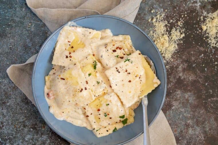 Ravioli in serving plate with spoon, and cheese sprinked on the side.