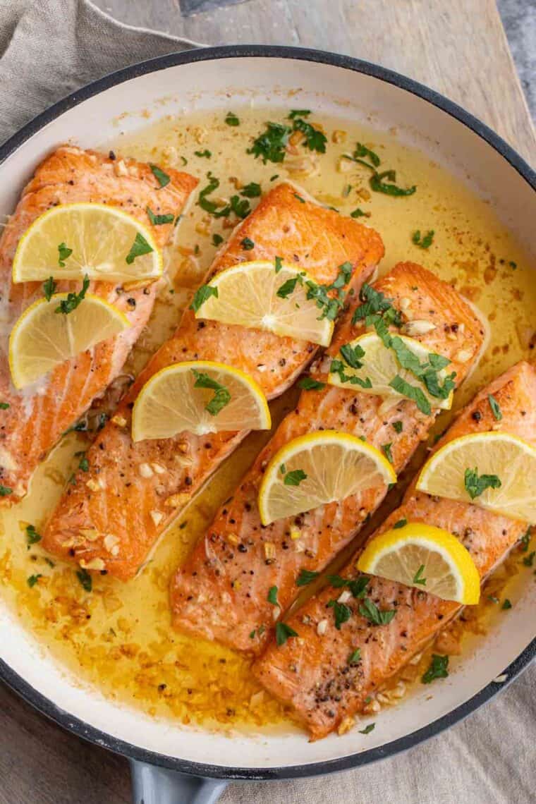 Close up of salmon with butter sauce inside of searing pan.