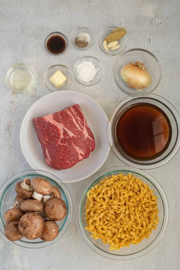 All ingredients needed to make beef and noodles. Oil, butter, onion, beef, mushrooms, egg noodles, beef broth, corn starch.
