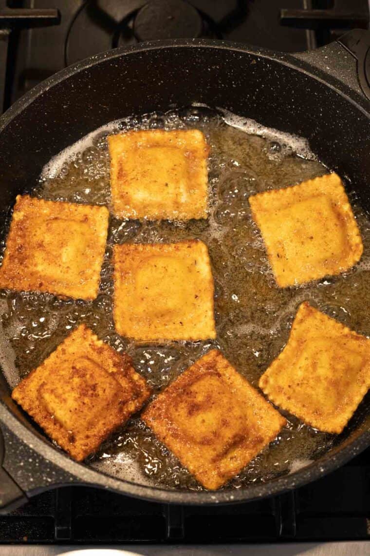 Cheesy ravioli being deep fried in a pan.