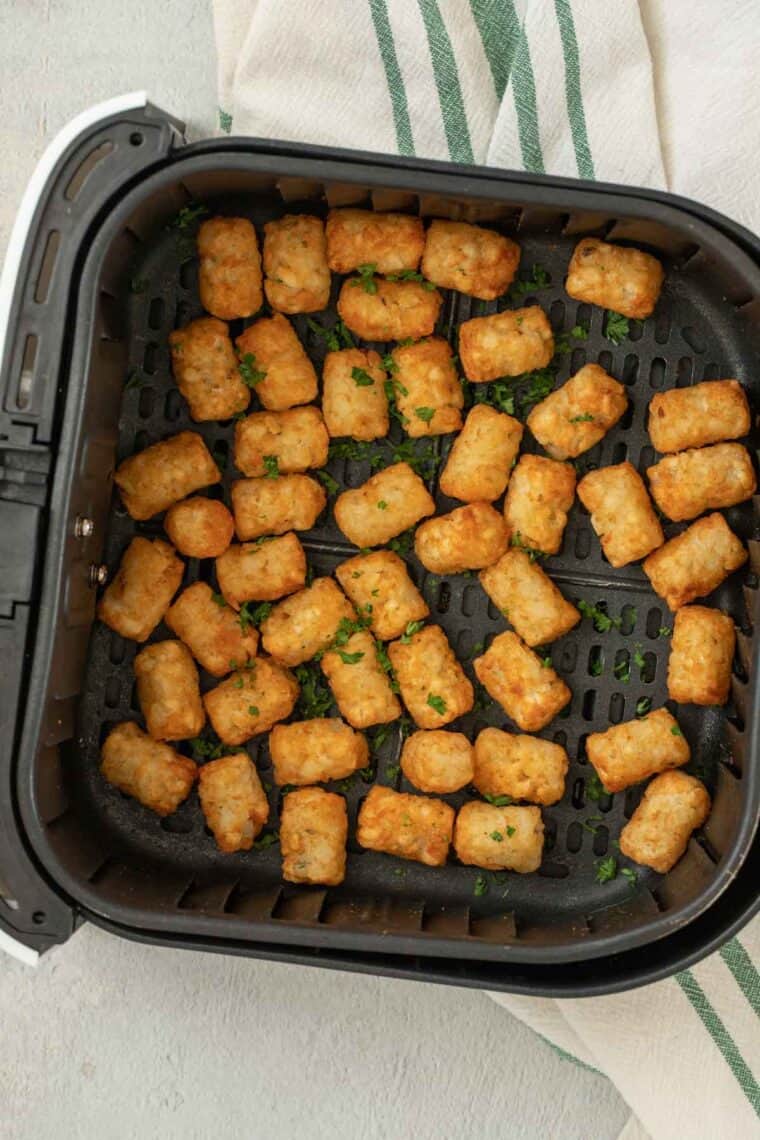 Tater tots in air fryer topped with greens.