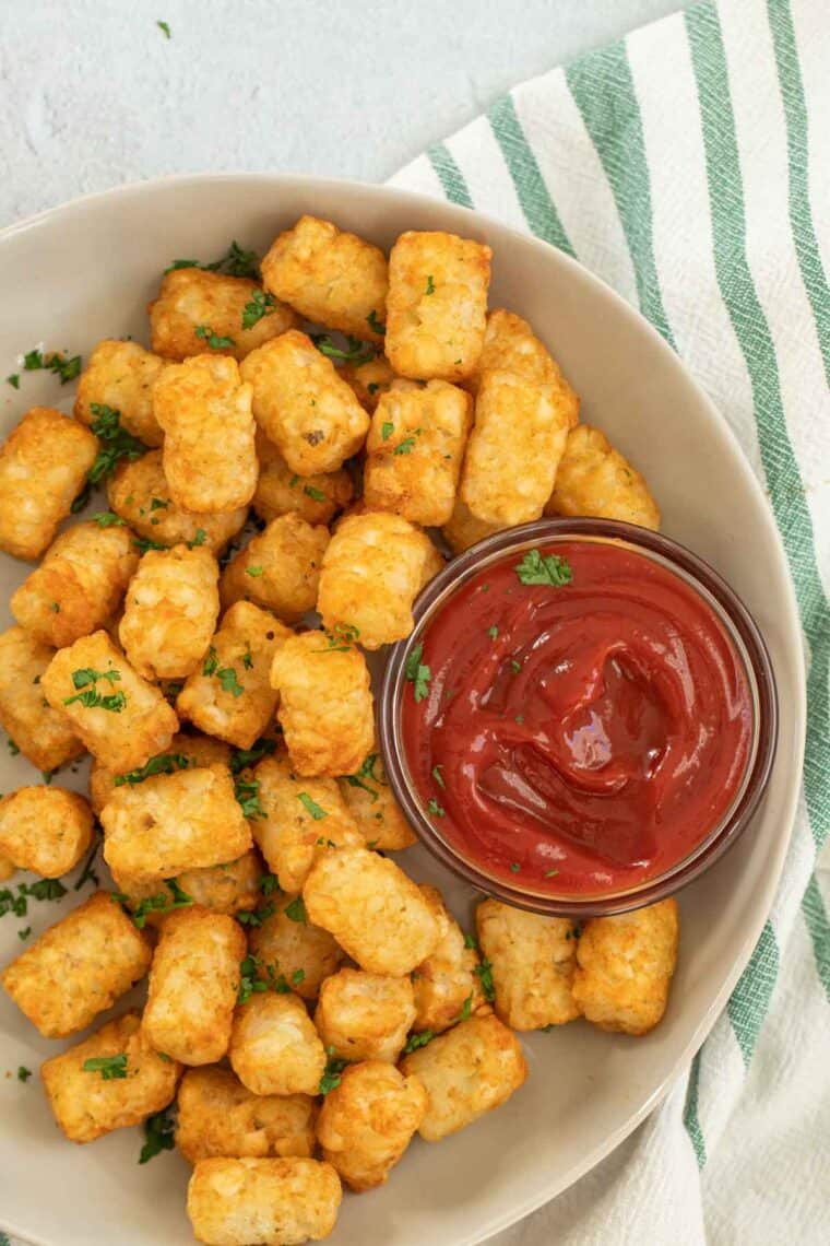 Cooked tater tots on a plate with a side of ketchup.