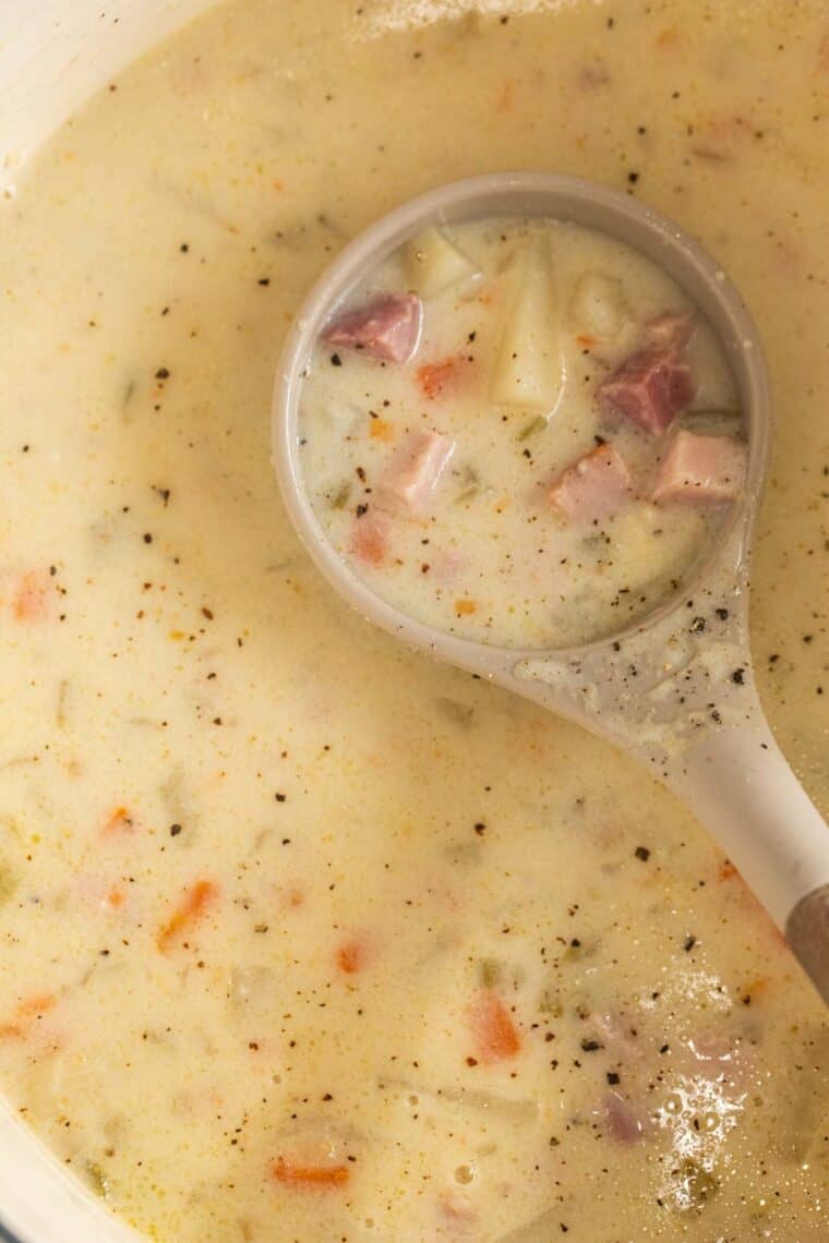 Up close of ham and soup in dutch oven being scopped with serving spoon.