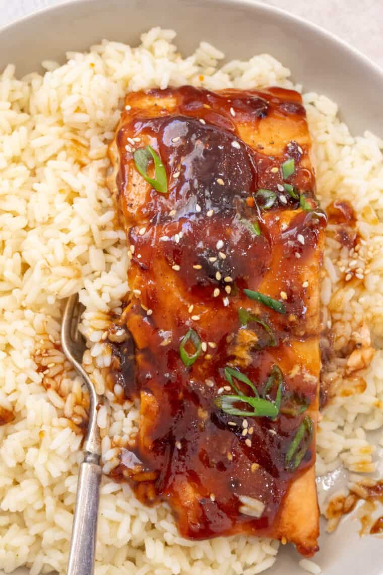 Close up of baked teriyaki salmon plated with rice topped with greens.