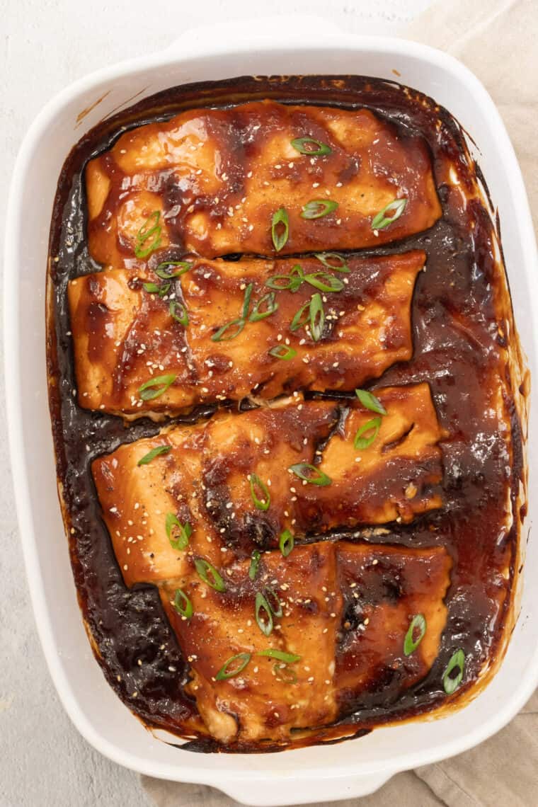 Teriyaki salmon fillet recipe in a pan topped with greens and sesame seeds.