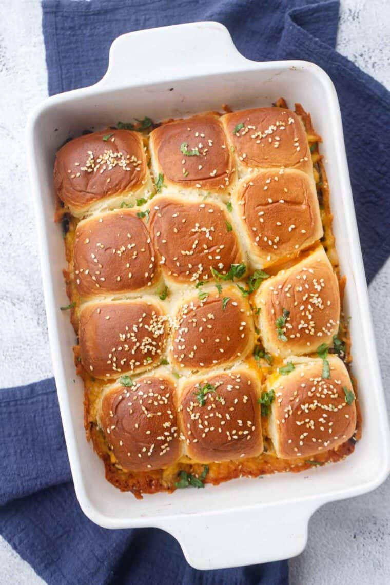 Cheeseburger sliders in a baking dish topped with sesame seeds and greens.