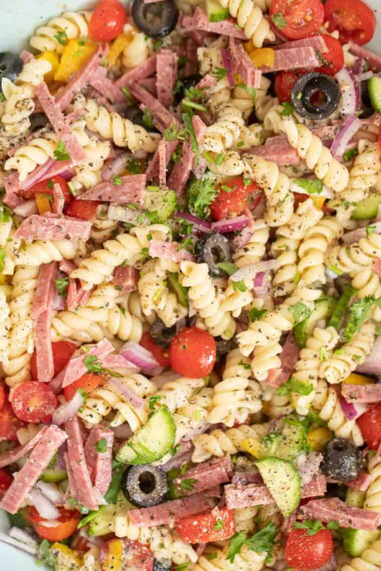 Pasta with salami, vegetable and dressing tossed in a large serving bowl.