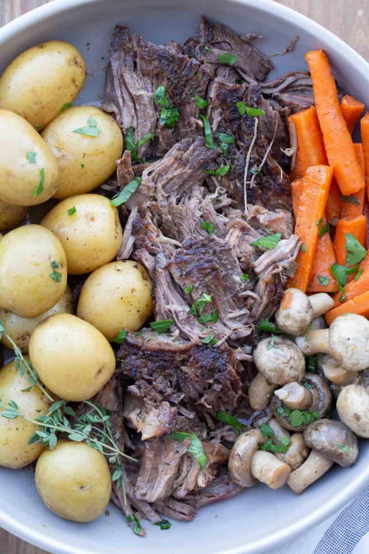 Close up of slow cooker pot roast recipe in serving plate with pulled chicken.