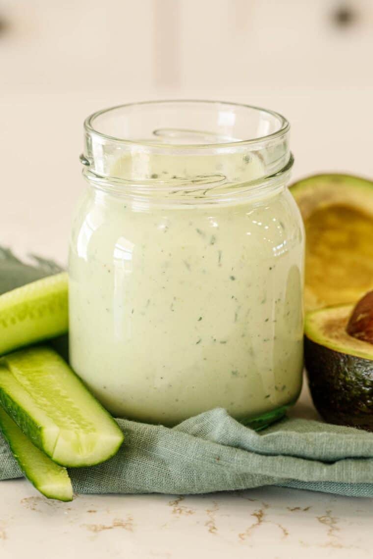 Avocado ranch in a jar with a side of a cut avocado and cucumber.