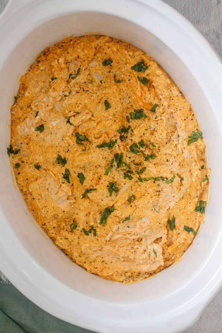 Finished buffalo chicken dip inside crockpot topped with greens.
