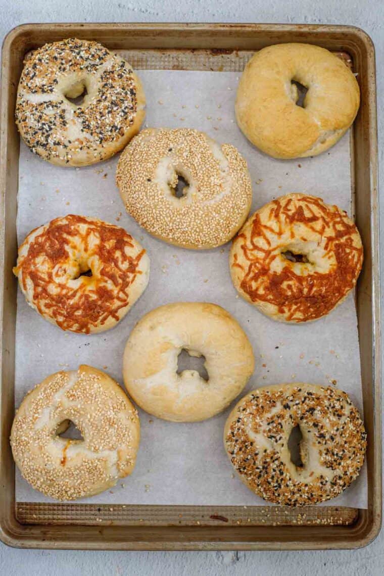 Various finished bagels topped with sesame seeds, everything seasoning, cheese, and plain bagels.