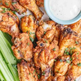 Close up image of wings on a serving plate with ranch and celery.