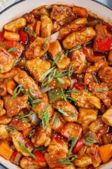 Chicken bites with bell vegetable and sauce in a skillet topped with green onion and sesame seeds.