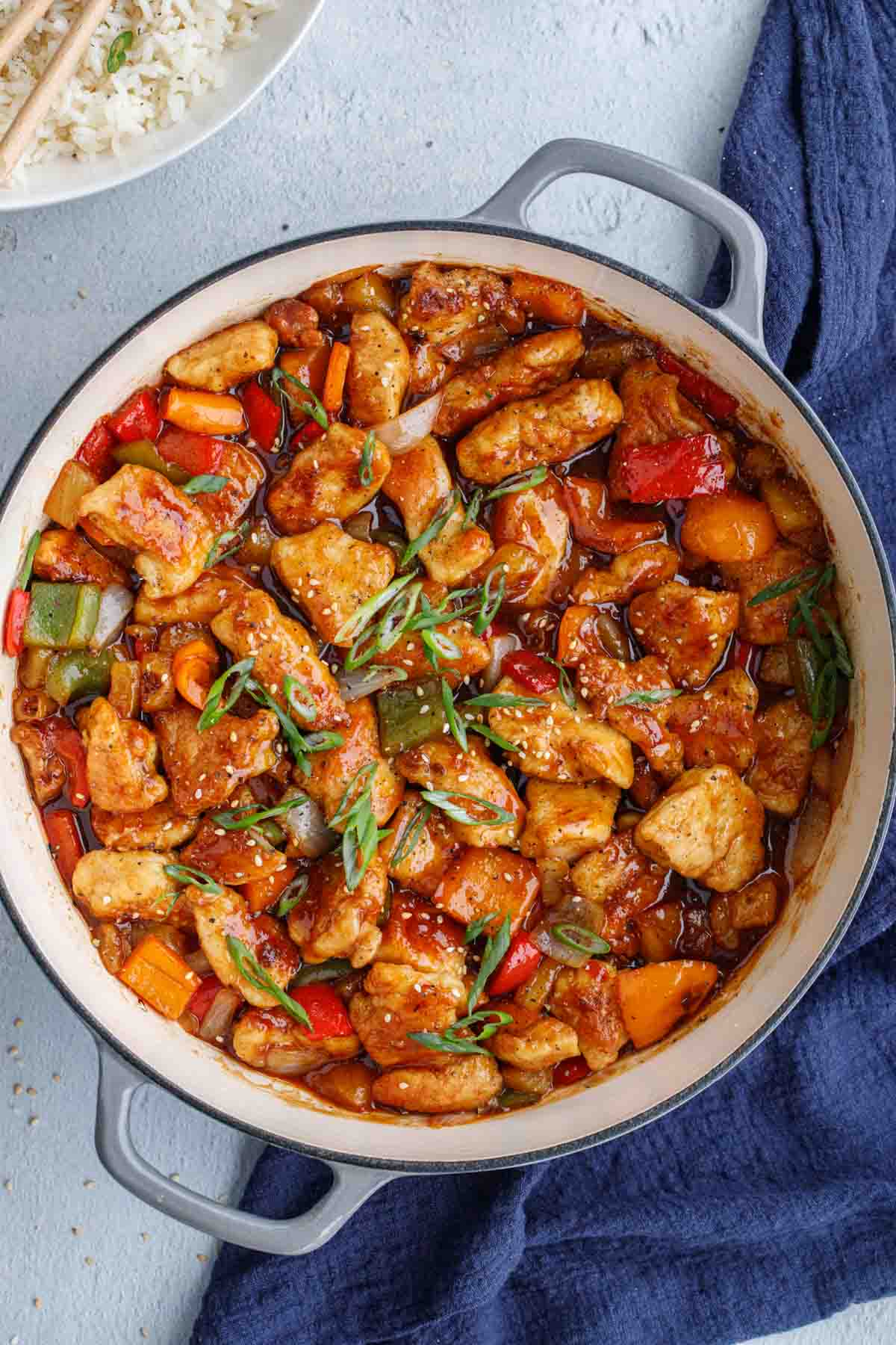 Sweet and sour chicken in skillet topped with greens.