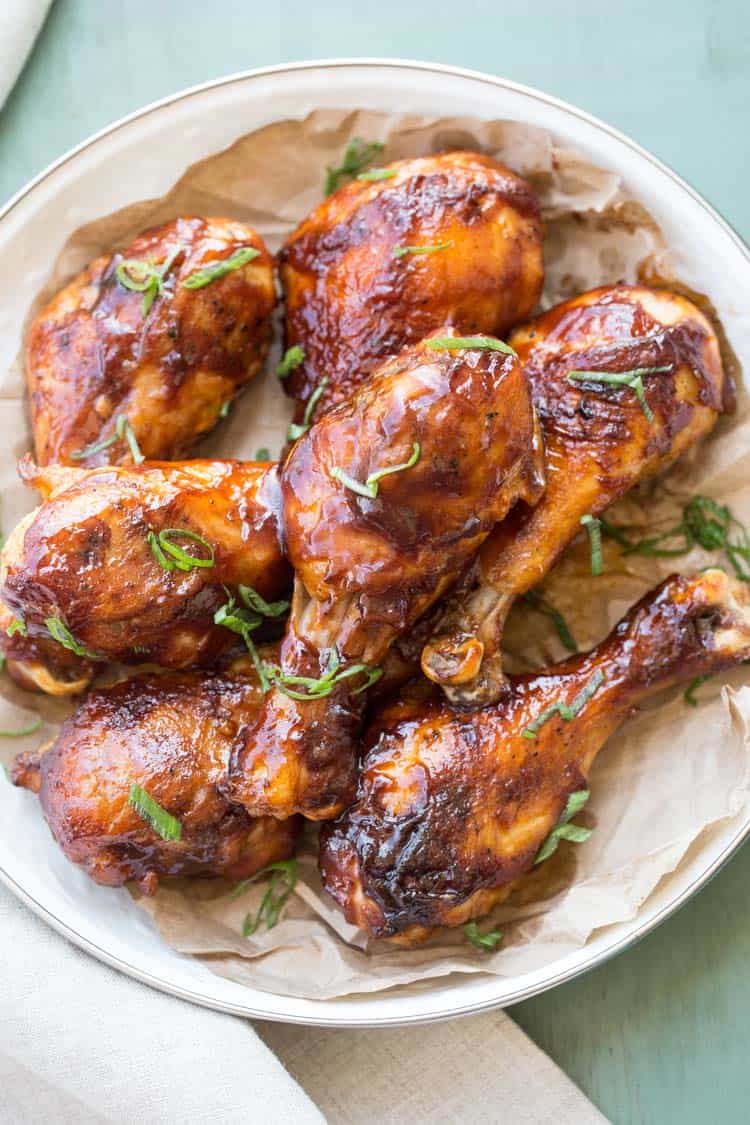 Baked BBQ chicken drumsticks in a bowl with topped with green onion.