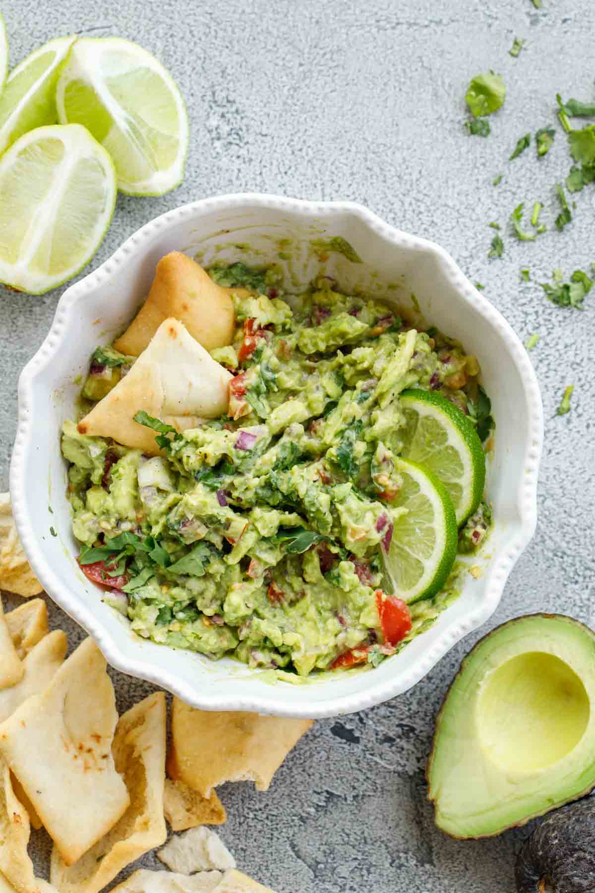 Easy guac recipe in a bowl sided with avocados, chips, and lime.