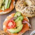 Salmon bagels topped with avocados, cappers, onions, tomatoes, and cucumbers.